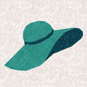 Op de afbeelding: Een turquoise zonnehoed met een brede rand en een donkerblauwe band. De kroon en rand van de hoed hebben verschillende texturen, met een patroon op de rand. De hoed staat tegen een bloemenachtergrond.