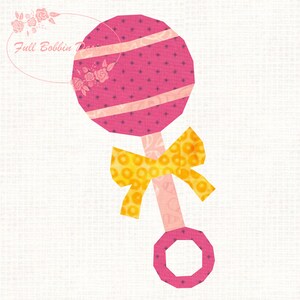 May include: A pink and yellow baby rattle design. The rattle features a round head with pink fabric, diagonal stripes, and a small star pattern. A yellow bow is tied below the head. The handle and ring are pink. The text "Full Bobbin Days" is in the upper left corner.