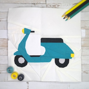 Könnte beinhalten: Ein Papierbastel-Scooter in Türkis und Weiß mit schwarzen Rädern und einem gelben Scheinwerfer. Der Roller befindet sich auf einem weißen Hintergrund mit Buntstiften und Garnrollen im Hintergrund.