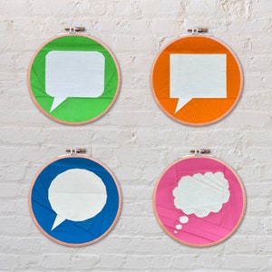 Puede incluir: Cuatro aros de bordado coloridos con burbujas de diálogo blancas en su interior. Los aros son verde, naranja, azul y rosa.