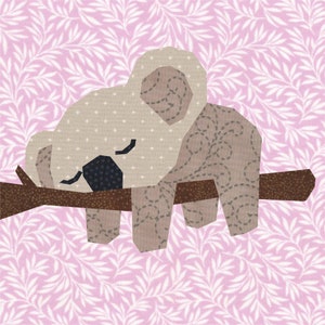 K&ouml;nnte beinhalten: Ein brauner und grauer Koalab&auml;r, der auf einem braunen Ast schl&auml;ft. Der Koala ist aus Stoff gefertigt und hat ein gesticktes Design.