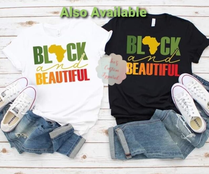 May include: Two t-shirts with the text "Black and Beautiful" in green, yellow, orange, and red. The text is overlaid on a silhouette of the continent of Africa. One t-shirt is white and the other is black.