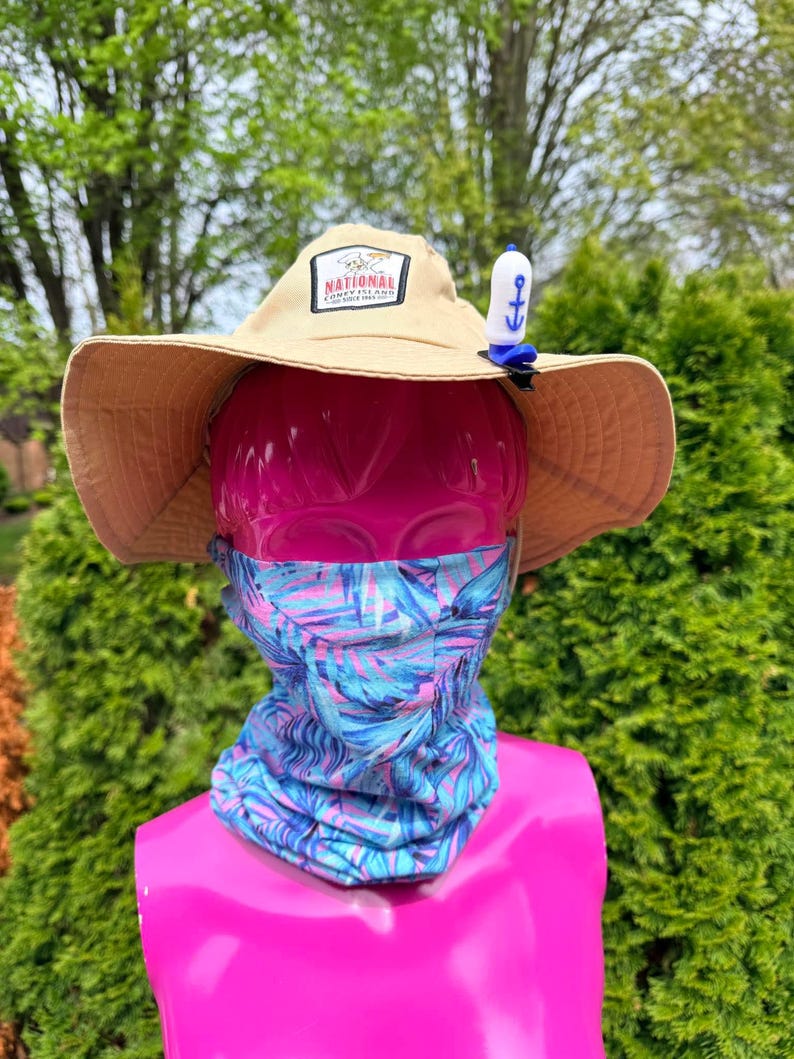 Puede incluir: Un sombrero para el sol de color beige con un parche que dice "National Coney Island Since 1966" se muestra en una cabeza de maniqu&iacute; rosa. El sombrero tiene un clip de ancla azul y blanco. Tambi&eacute;n se usa un polaina para el cuello con estampado azul, rosa y blanco.