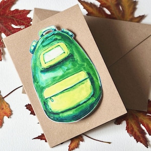 Könnte beinhalten: Aquarellillustration eines grünen Rucksacks mit gelben Akzenten, platziert auf einer braunen Karte mit passendem Umschlag. Das Bild ist von bunten Herbstblättern umgeben und erzeugt ein saisonales Thema.
