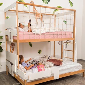 May include: A wooden bunk bed with a white frame and a rope net on the top bunk. The top bunk has a pink mattress and the bottom bunk has a white mattress. The wall is decorated with giraffe and leaf decals.
