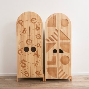 May include: Two wooden cabinets with arched tops and doors. The cabinet on the left has a design of letters and numbers carved into the doors. The cabinet on the right has a design of geometric shapes carved into the doors.