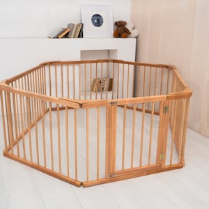 Pu&ograve; includere: Un box per bambini esagonale in legno con un cancello. Il box &egrave; realizzato in legno naturale e ha una finitura marrone chiaro. Il cancello &egrave; incernierato e ha un chiavistello.