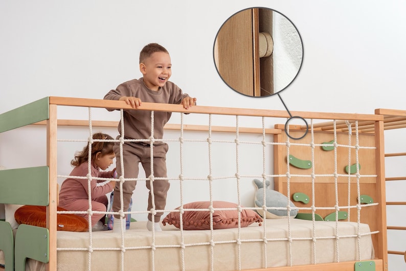 Pu&ograve; includere: Un letto per bambini in legno con parete da arrampicata, rete di corda e scala. La struttura del letto &egrave; marrone chiaro con accenti verdi. Due bambini giocano sul letto. Il letto ha un materasso color crema e un cuscino rosa.
