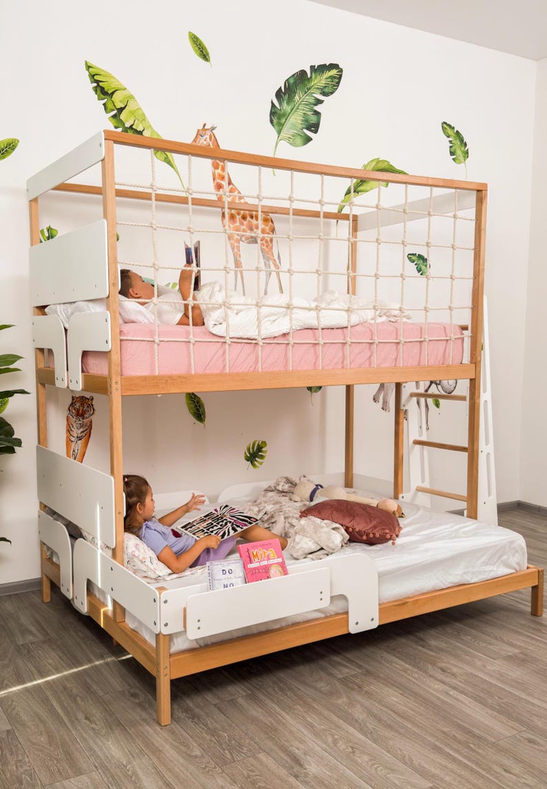 May include: A wooden bunk bed with a white frame and a rope net on the top bunk. The top bunk has a pink mattress and the bottom bunk has a white mattress. The wall is decorated with giraffe and leaf decals.
