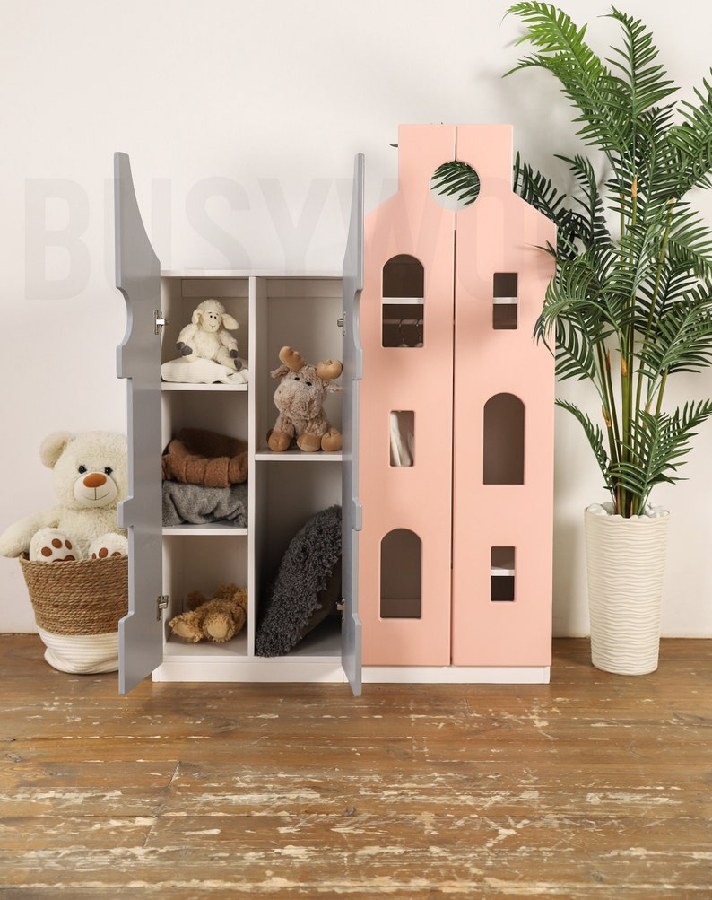 Op de afbeelding: Een grijs en roze houten speelhuis met een deur die open kan. Het huis heeft planken binnenin en is versierd met ramen en een dak. Het huis staat op een houten vloer.