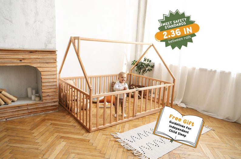 May include: A natural wood house-shaped toddler bed with a slatted fence. The bed frame has a roof and a gate. The text on the image says "MEET SAFETY STANDARDS 2.36 IN between rails" and "Free Gift Guidelines for Independent Child Sleep".
