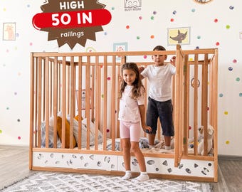 May include: A light-colored wooden floor bed with vertical railings and a white base featuring geometric cutouts. A brown starburst graphic on the bed displays the text EXTRA HIGH 50 IN railings. The bed includes a hinged gate section.