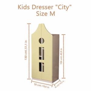 Op de afbeelding: Drie houten kinderkledingkasten in verschillende maten, met de labels "Kids Dresser "City" Size S", "Kids Dresser "City" Size M" en "Kids Dresser "City" Size L". De kasten zijn vormgegeven als huisjes met een afgerond dak en twee deuren. De kleine kast is lichtblauw, de middelste is geel en de grote is groen.