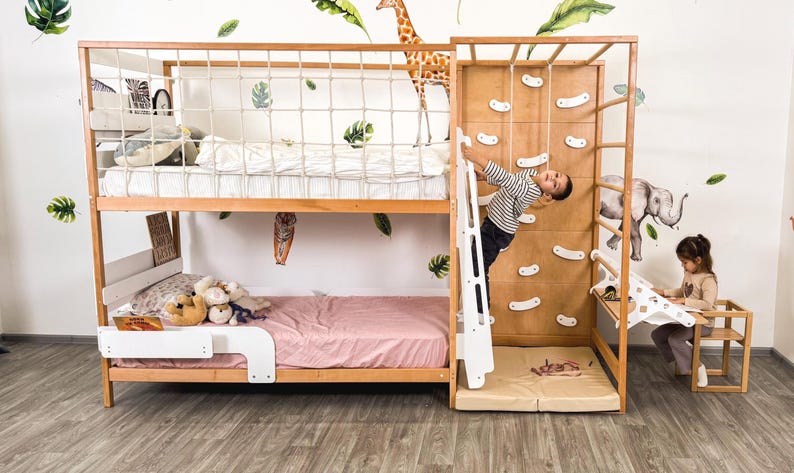 Pu&ograve; includere: Un letto a castello in legno con una parete da arrampicata e una scala. Il letto ha una struttura marrone chiaro con una rete di sicurezza bianca sulla cuccetta superiore. Un bambino sta arrampicando sul muro. La stanza &egrave; decorata con adesivi murali a forma di foglie e animali.