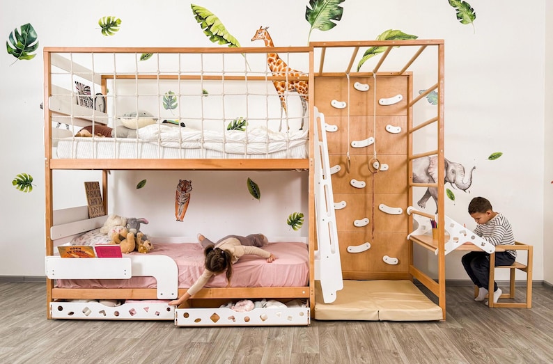 Pu&ograve; includere: Un letto a castello in legno con una parete da arrampicata, una scala e una rete di corda. Il letto ha una struttura in legno chiaro con un materasso rosa sulla cuccetta inferiore. Un bambino sta giocando sul letto. Sono visibili adesivi murali a tema giungla.