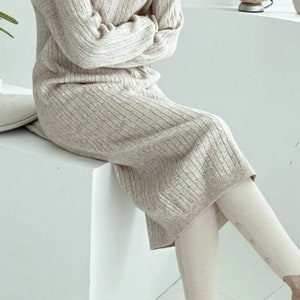 Peut inclure: Une robe pull beige en maille c&ocirc;tel&eacute;e avec des manches longues et une longueur midi. La robe est associ&eacute;e &agrave; des leggings blanc cass&eacute;. Les manches sont crois&eacute;es sur la poitrine. Les leggings ont des boutons d&eacute;coratifs sur le c&ocirc;t&eacute;.
