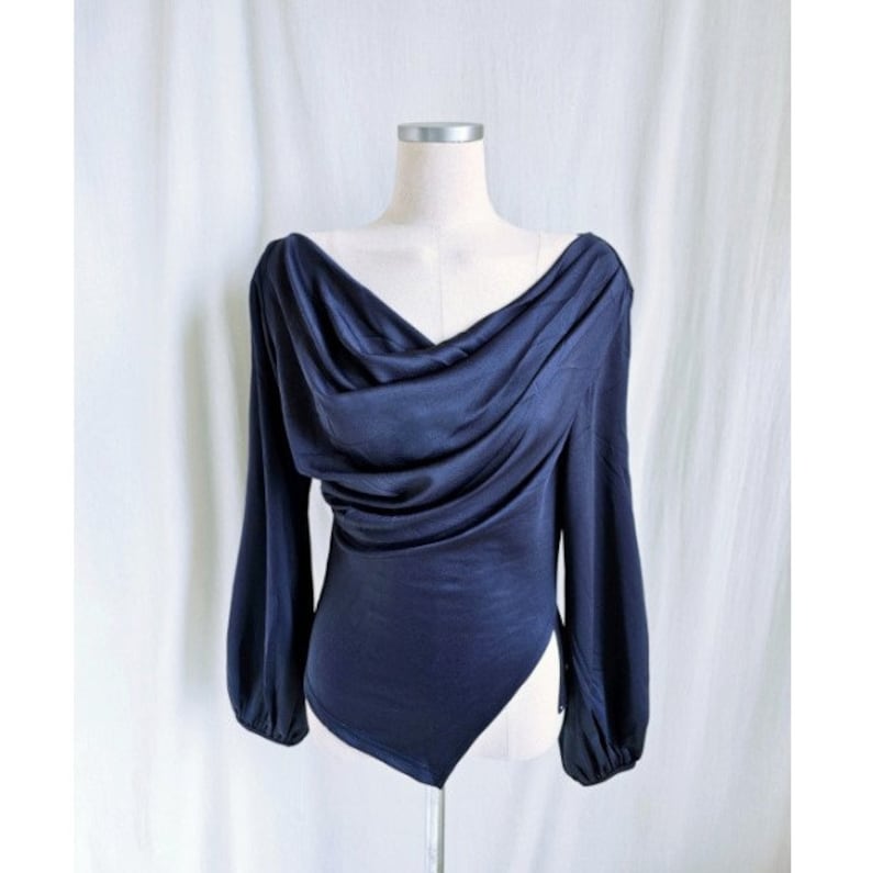 May include: Navy blue bodysuit with a draped cowl neckline and long sleeves. The fabric has a slight sheen, and the sleeves gather at the wrists. The garment is displayed on a mannequin against a white backdrop.
