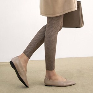 Puede incluir: Bailarinas color topo con punta y suela negra. Se combinan con leggings de punto acanalado en un tono marr&oacute;n similar. Un abrigo beige y un bolso marr&oacute;n completan el conjunto.