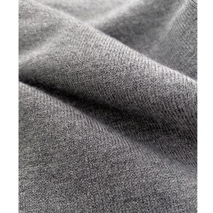 May include: Close-up of a gray knit fabric with visible texture and folds. The fabric appears soft and has a subtle sheen, suggesting a comfortable material. The image highlights the detailed weave and the overall color.