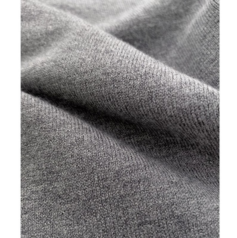 May include: Close-up of a gray knit fabric with visible texture and folds. The fabric appears soft and has a subtle sheen, suggesting a comfortable material. The image highlights the detailed weave and the overall color.