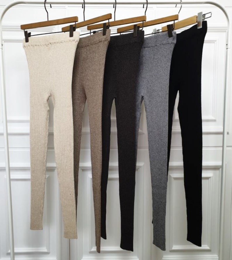 Puede incluir: Cinco pares de leggings de punto acanalado en una variedad de colores neutros cuelgan de perchas de madera. Los colores incluyen beige, marr&oacute;n, gris oscuro, gris claro y negro. Los leggings se muestran sobre un fondo blanco.
