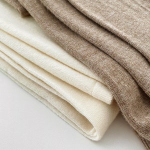 May include: Close-up of folded socks in cream and tan. The socks are made of a soft, textured material. The cream-colored socks are stacked in a neat pile, while the tan socks are folded on top.