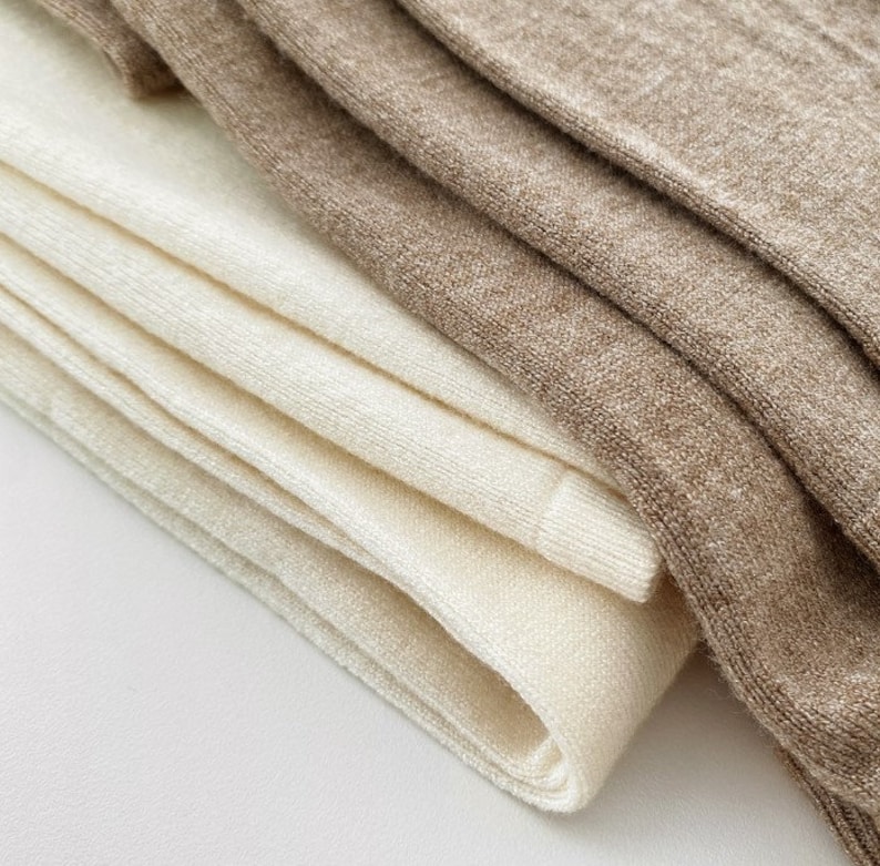 May include: Close-up of folded socks in cream and tan. The socks are made of a soft, textured material. The cream-colored socks are stacked in a neat pile, while the tan socks are folded on top.