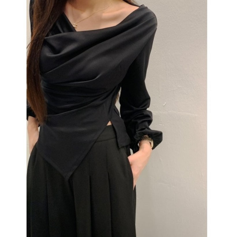 May include: Black long-sleeve top with a draped cowl neckline and a split hem. The top is paired with black pleated pants. The outfit is a sleek, monochromatic ensemble.