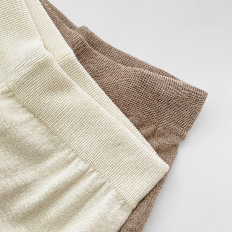 May include: Close-up of two pairs of leggings. One pair is a light cream color, and the other is a muted brown. Both pairs have a ribbed waistband and a soft, textured fabric.
