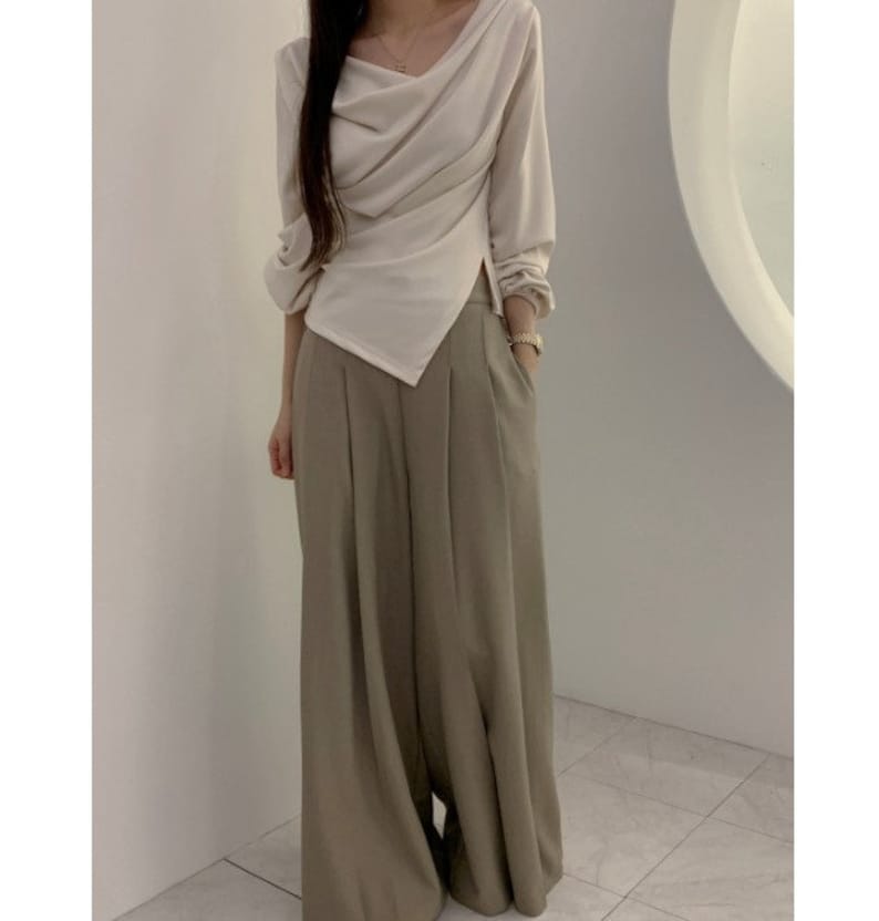 May include: A cream-colored long-sleeve top with a draped neckline and asymmetrical hemline. Paired with wide-leg, olive-green trousers. The outfit is a modern, minimalist style, suitable for various occasions.