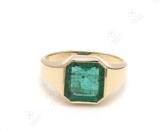 May include: A gold ring with a large, emerald green gemstone set in a square shape. The ring has a simple, classic design.