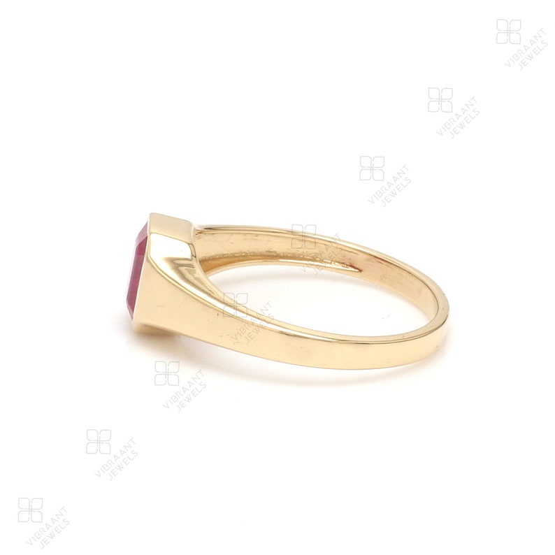 May include: A gold ring with a red gemstone. The ring is set in a simple, classic style.