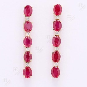 Puede incluir: Pendientes de oro con una disposición vertical de rubíes rojos ovalados. Cada rubí está acentuado con un pequeño diamante brillante. Diseño clásico y sofisticado, ideal para ocasiones especiales.