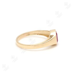 May include: A gold ring with a red gemstone set in a square shape. The ring is simple and elegant.