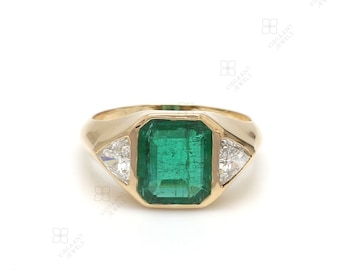 May include: A gold ring with a large emerald green gemstone surrounded by two smaller triangular diamonds.