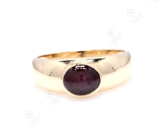 May include: A gold ring with a deep red gemstone set in a bezel setting. The ring has a smooth, rounded band.