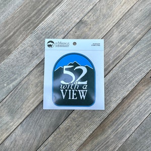May include: A blue and green sticker with the text "52 with a VIEW" and a mountain range graphic. The sticker is from "of Moose & Mountain" and is an "ADHESIVE STICKER".