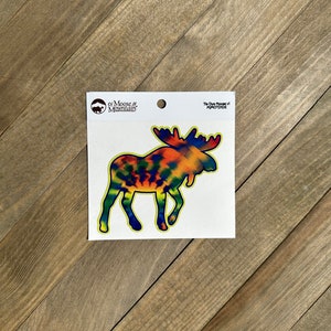 May include: Tie Dye Moose vinyl sticker with a yellow outline. The sticker is on a white background with the Moose & Mountain logo and the text "Tie Dye Moose v1" in black.