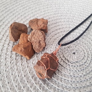 Pode incluir: Um pingente de pedra marrom envolto em fio de cobre, pendurado em um cordão preto. O pingente é cercado por quatro pedras marrons menores.