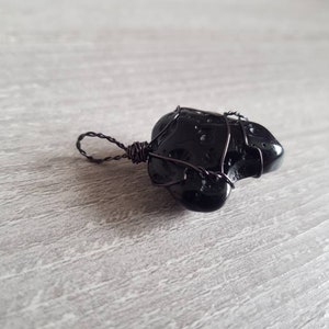 May include: Black obsidian stone pendant wrapped in black wire. The pendant has a unique, irregular shape and is perfect for a minimalist jewellery design.