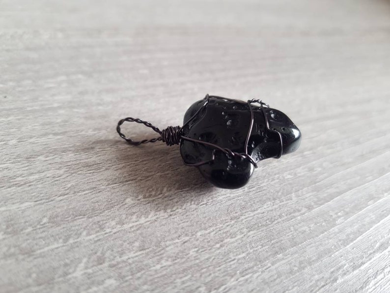 May include: Black obsidian stone pendant wrapped in black wire. The pendant has a unique, irregular shape and is perfect for a minimalist jewellery design.