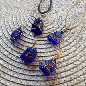 May include: Five blue glass pendants wrapped in wire, each with a different length of chain. The pendants are on a woven surface.