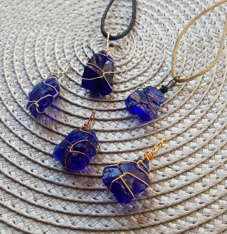 May include: Five blue glass pendants wrapped in wire, each with a different length of chain. The pendants are on a woven surface.