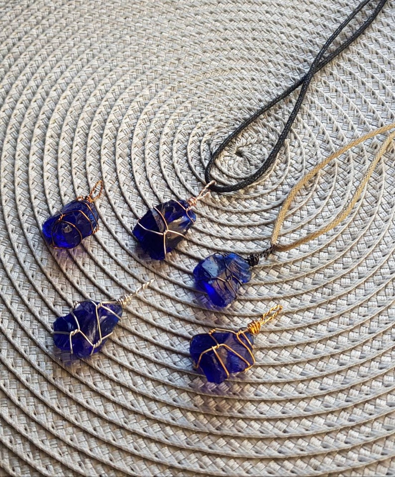May include: Four necklaces with blue glass pendants wrapped in gold wire. The pendants are different shapes and sizes. The necklaces are on a woven placemat.