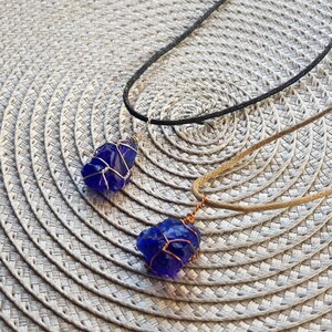 May include: Two necklaces with blue glass pendants wrapped in copper wire. The necklaces are on a woven placemat.