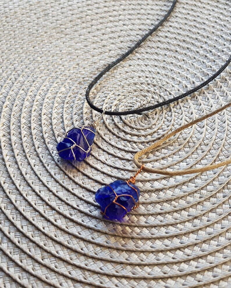 May include: Two necklaces with blue glass pendants wrapped in copper wire. The necklaces are on a woven placemat.