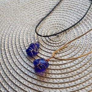 May include: Two necklaces with blue glass pendants wrapped in wire. One necklace has a black cord and the other has a brown cord.