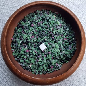 May include: A wooden bowl filled with green and pink gemstone chips. The chips are small and irregular in shape. There is a small white square in the centre of the bowl.