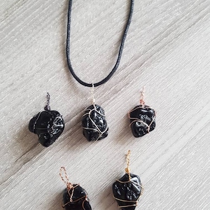 May include: Five black obsidian pendants wrapped in silver, gold, and copper wire. The pendants are hanging from black cords.