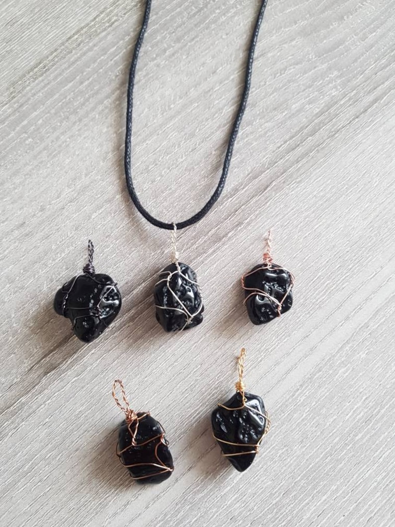 May include: Five black obsidian pendants wrapped in silver, gold, and copper wire. The pendants are hanging from black cords.